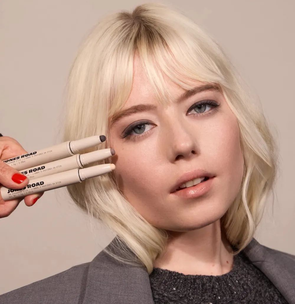 Model holding three Jones Road eyeshadow sticks to her temple